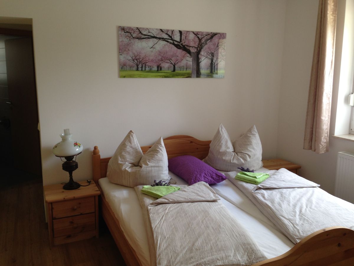 Zimmer mit Doppelbett aus Holz, links ein Nachtisch mit Lampe, an der Wand ein Bild