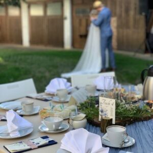 gedeckter Tisch im Garten, im Hintergrund ein Hochzeitspaar