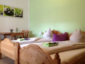 Zimmer mit zwei einzelnen Betten aus Holz, im Hintergrund ein Tisch mit Stuhl und eine grüne Wand